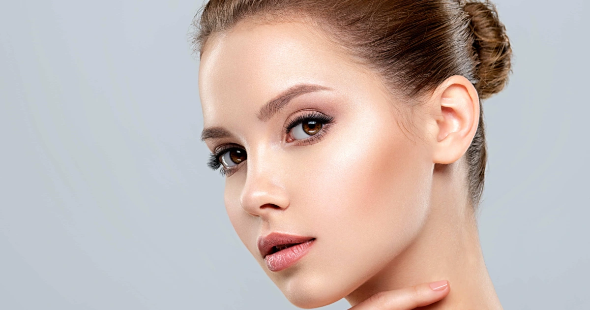 Studio portrait of a woman with clear skin, elegant makeup, and a neat bun, gently touching her neck and collarbone, representing Skin Rejuvenation in Allen, TX.
